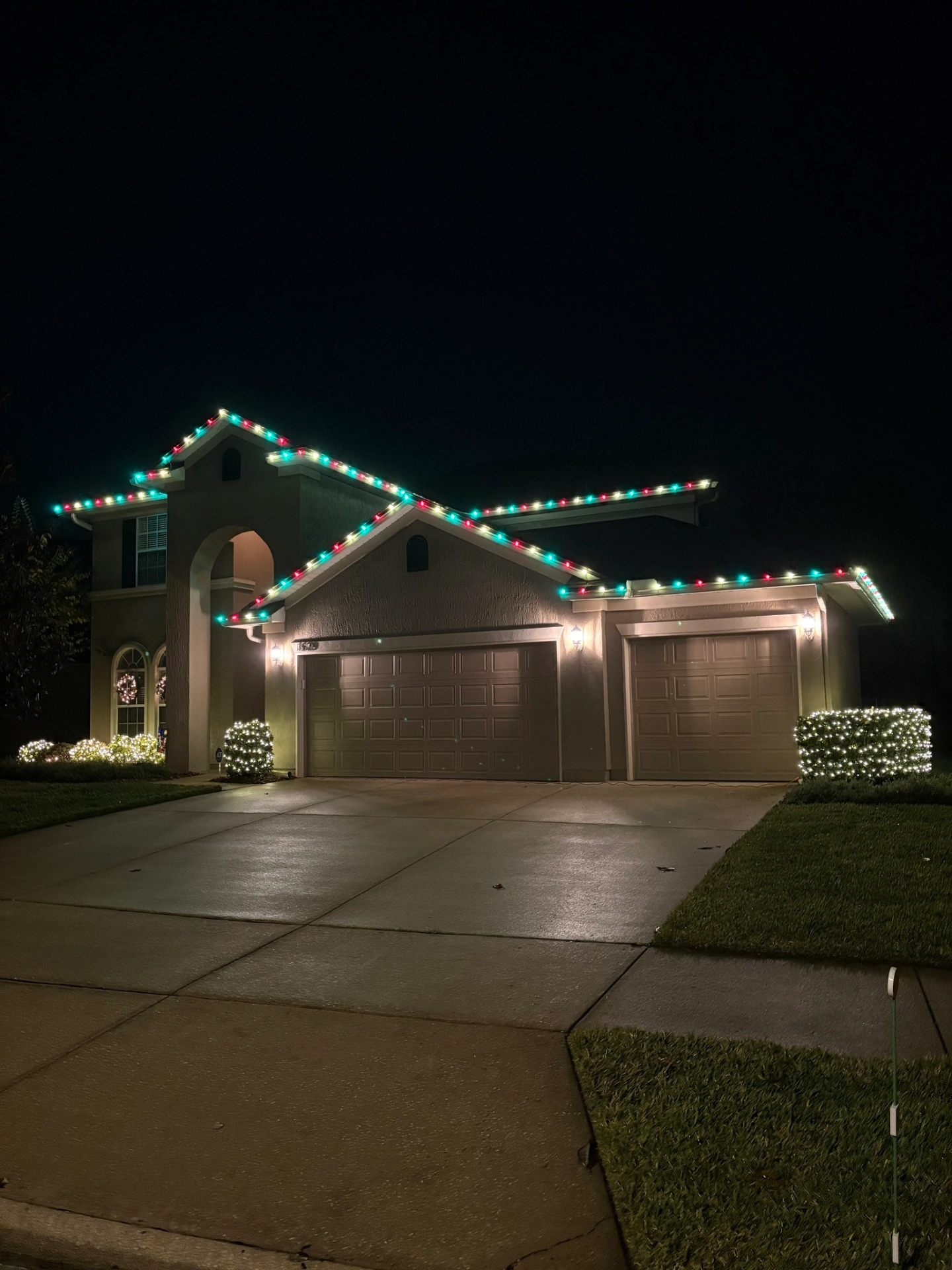 Red and green holiday lights with illuminated bushes
